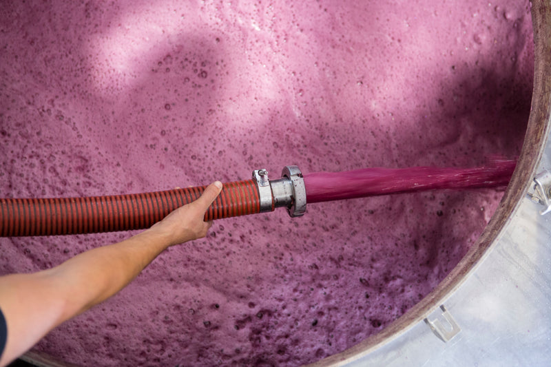 Foto einer Hand die einen Schlauch über einen Edelstahltank hält um den Vorgang des sogenannten Pump Overs durchzuführen.