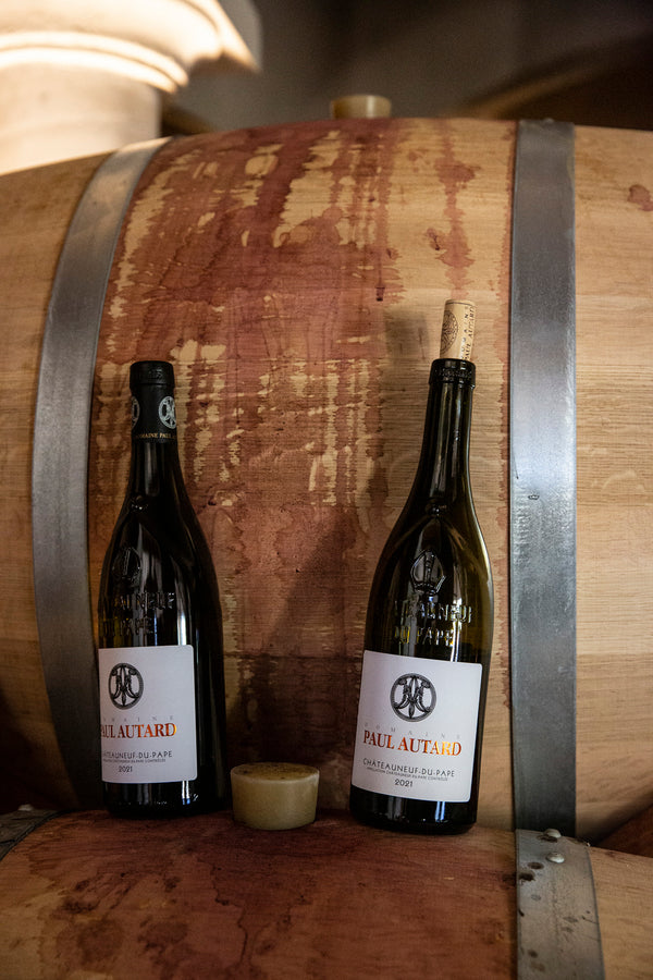 Zwei Flaschen Wein vom Weingut Paul Autard stehen auf einem Faß im Keller und lehnen an einem Zweiten.
