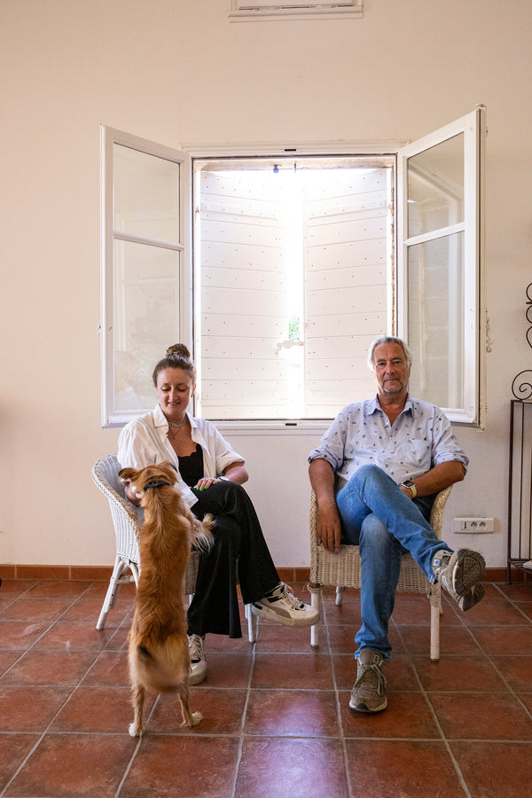 Jean-Paul Autard und seine Tochter sitzen auf zwei weißen Korbstühlen im Weingut. Ein Hund springt an der Tochter hoch.
