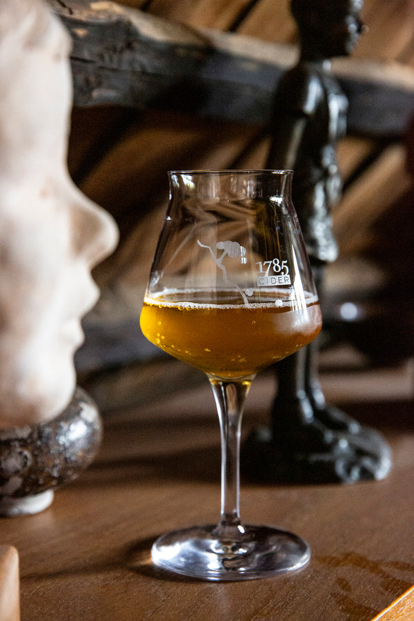 Ein Glas Cider des Produzenten 1785 Cider steht zwischen kleinen Skulpturen in schöner Beleuchtung.