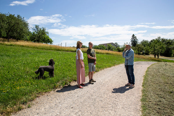 Anna Flohr und Guido Walter von walter&sohn im Gespräch mit Patrick Mann von 1785 Cider auf einem Schotterweg zwischen Apfelbäumen.