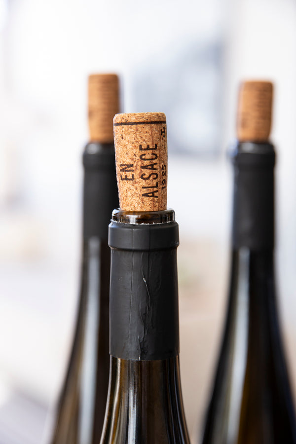 Aufnahme von drei geöffneten Flaschen Wein, in die die Korken zurückgesteckt wurden Auf dem Vordersten steht "En Alsace"