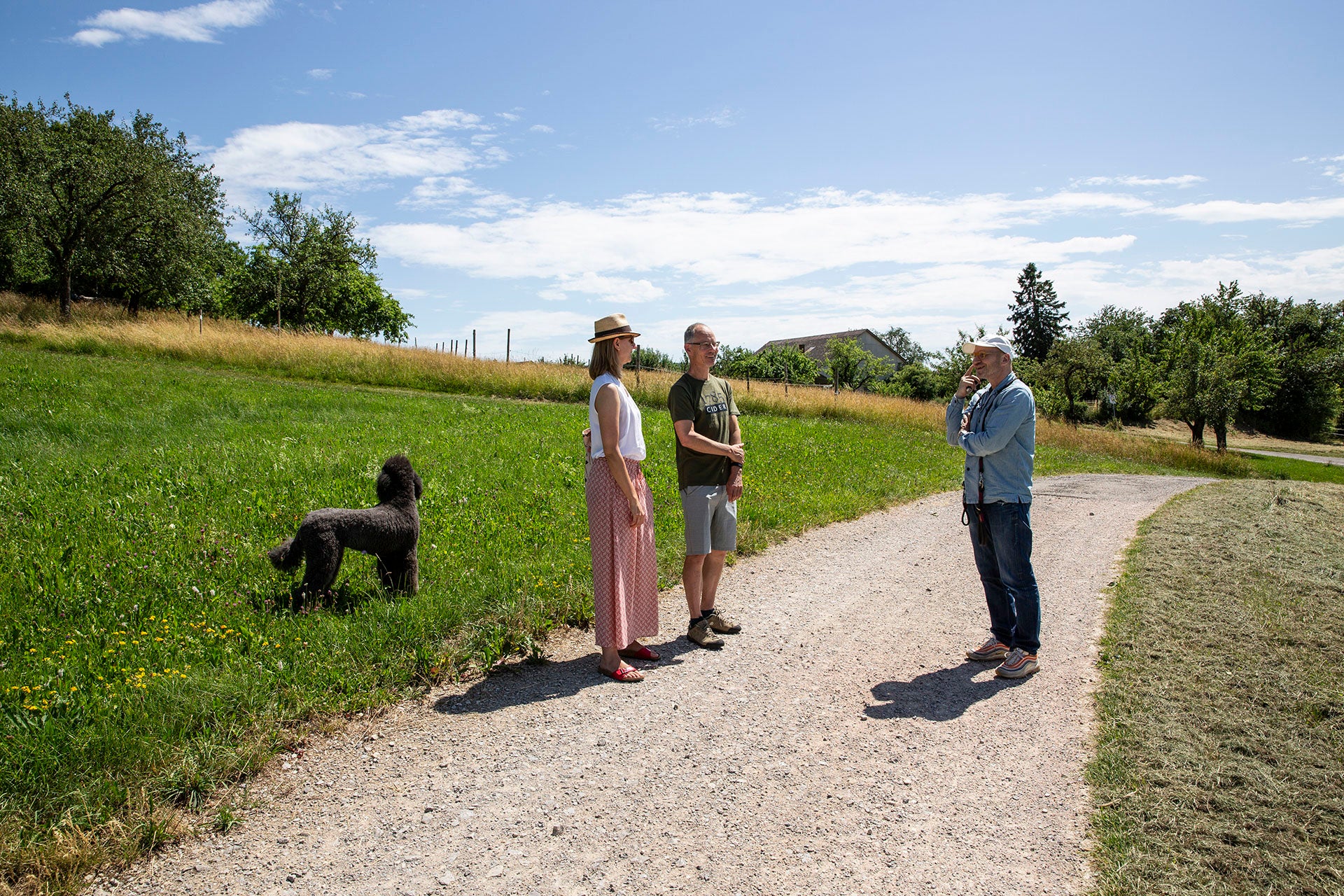 Anna Flohr und Guido Walter von walter&sohn im Gespräch mit Patrick Mann von 1785 Cider auf einem Schotterweg zwischen Apfelbäumen.